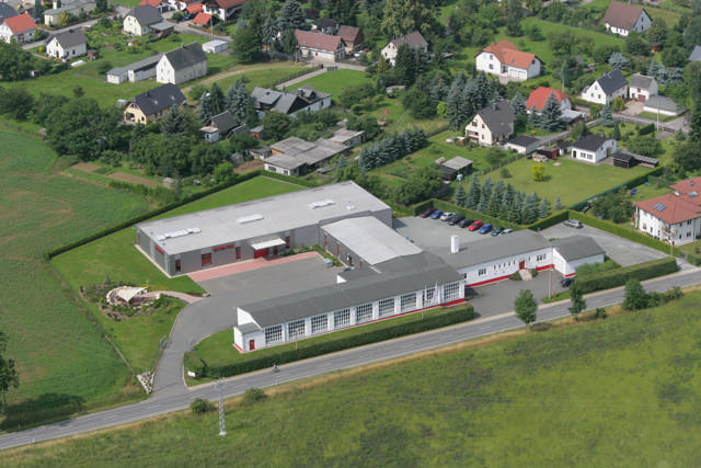 Luftaufnahme des Röckelein GmbH Firmenkomplexes, umgeben von ländlichen Wohnhäusern und Grünflächen, mit modernen Industriegebäuden und Parkplätzen.